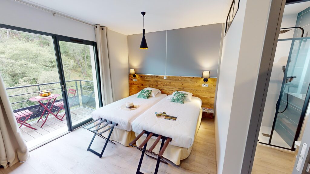 Chambre d'hôtel avec lit double, tête de lit en bois, lampes de chevet et balcon ouvert sur la verdure