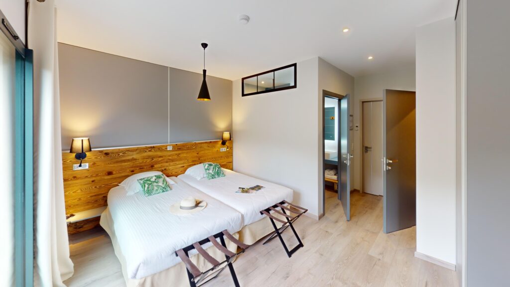 Intérieur de la chambre d'hôtel avec lit blanc, suspension noire, porte-bagages et accès à la salle de bain