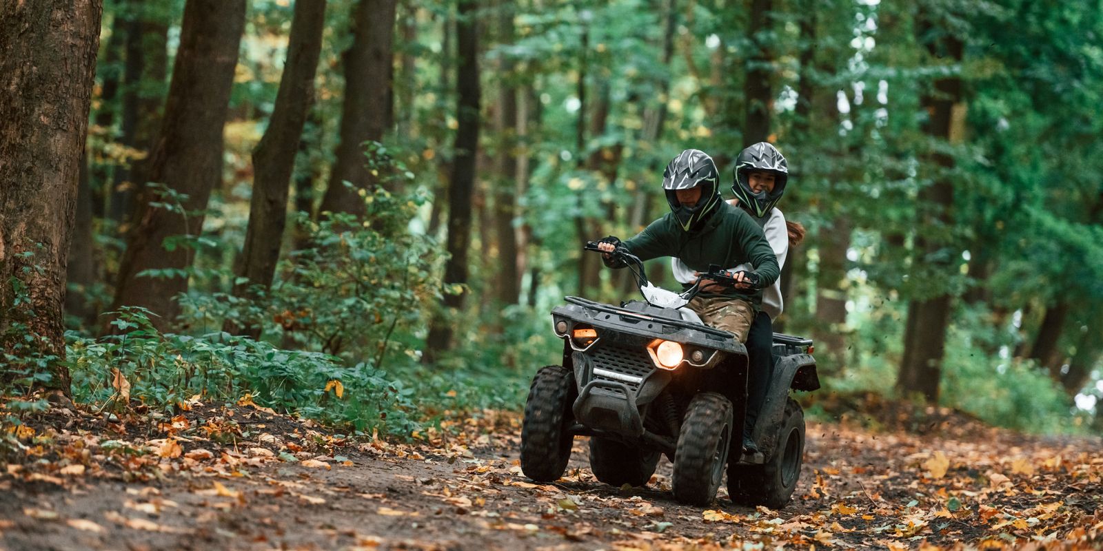 Duo en quad sur un chemin forestier couvert de feuilles